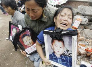 A mother (R) holding a portrait of her 12-year-old son Feng Junwei cries next to the ruins of destroyed Fuxing primary school in the earthquake-hit Wufu town of Mianzhu county, Sichuan province May 21, 2008.[Agencies] 